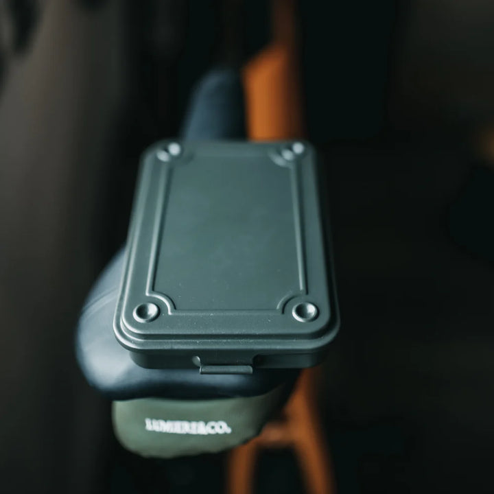 Closed Moss Green TOYO T-152 Steel Toolbox resting on a bicycle saddle, highlighting its portable, flat EDC profile.
