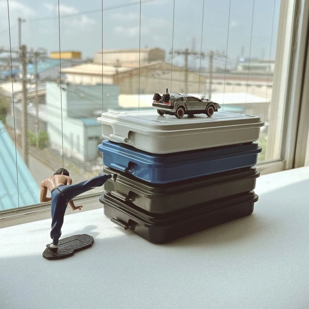 Stack of slim TOYO T-152 Steel Toolboxes on a desk with action figures, showing them as interlocking desktop organizers.