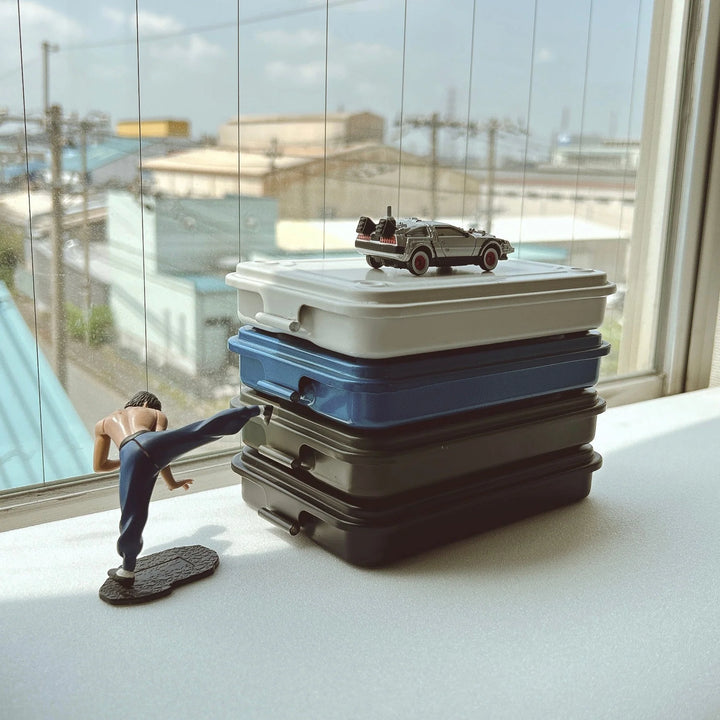Stack of slim TOYO T-152 Steel Toolboxes on a desk with action figures, showing them as interlocking desktop organizers.