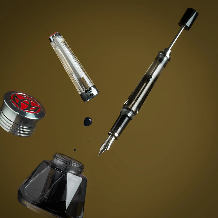 TWSBI Vac700R Fountain Pen - Clear, ink bottle, and cap on a brown background