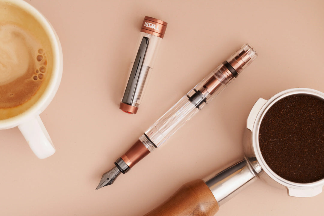 Creative flat lay of the TWSBI Diamond 580ALR Affogato fountain pen arranged on a warm beige surface alongside a ceramic espresso cup and a portafilter filled with fresh coffee grounds, highlighting its coffee-inspired design.