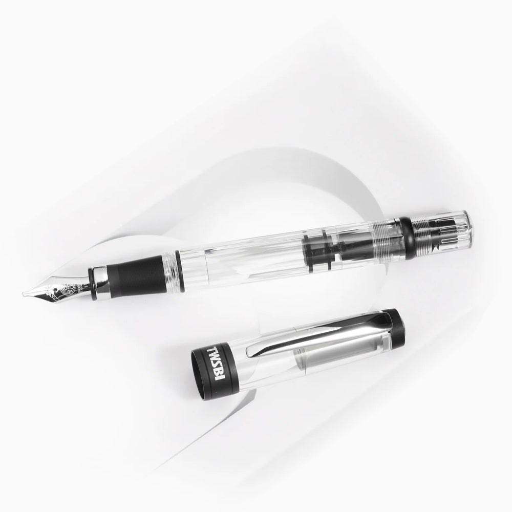 Top-down view of the uncapped TWSBI Diamond 580ALR Black fountain pen and its clear cap resting on a white curved display stand, detailing the internal piston mechanism and matte black cap band.