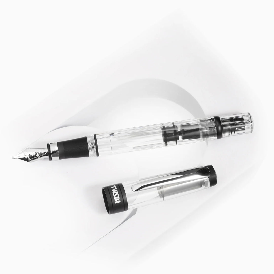 Top-down view of the uncapped TWSBI Diamond 580ALR Black fountain pen and its clear cap resting on a white curved display stand, detailing the internal piston mechanism and matte black cap band.