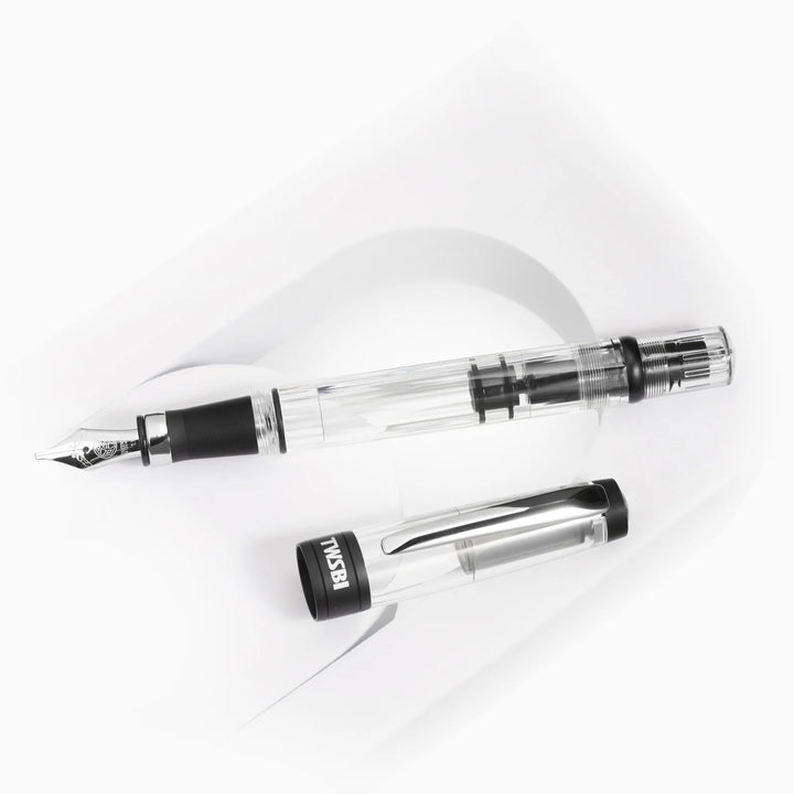 Top-down view of the uncapped TWSBI Diamond 580ALR Black fountain pen and its clear cap resting on a white curved display stand, detailing the internal piston mechanism and matte black cap band.