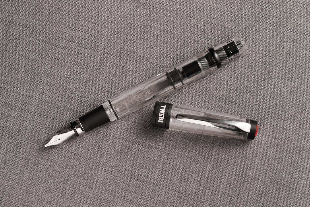 Uncapped TWSBI Diamond 580ALR Black fountain pen and cap resting on a textured grey woven fabric, showcasing the industrial contrast between the clear demonstrator resin, silver nib, and matte black ribbed aluminum accents.