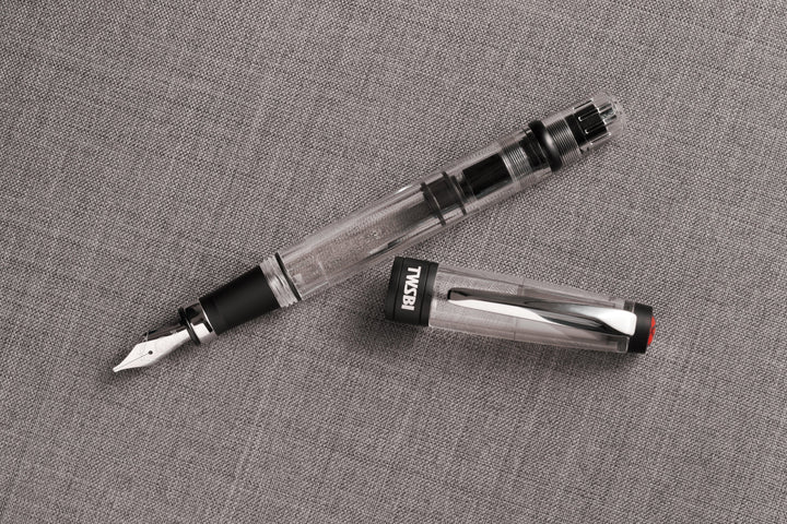 Uncapped TWSBI Diamond 580ALR Black fountain pen and cap resting on a textured grey woven fabric, showcasing the industrial contrast between the clear demonstrator resin, silver nib, and matte black ribbed aluminum accents.