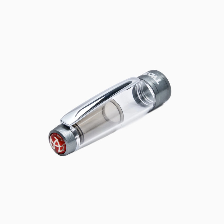 Close-up, angled view of the detached clear cap for the TWSBI Diamond 580ALR Nickel Gray fountain pen resting on a pure white background. The image details the transparent resin, polished silver pocket clip, matte nickel-gray cap band with the 'TWSBI' logo, and the inset red finial on top.
