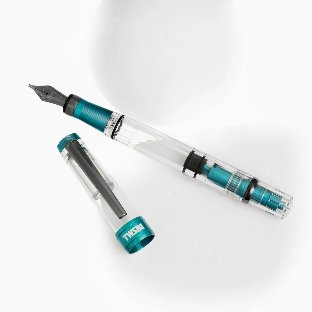 Artistic display of the TWSBI Diamond 580ALR Caribbean Blue fountain pen and cap resting near white geometric shapes, showing the internal blue piston mechanism and sleek black titanium clip.