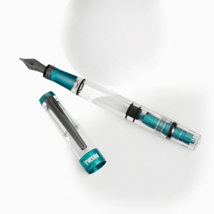 Artistic display of the TWSBI Diamond 580ALR Caribbean Blue fountain pen and cap resting near white geometric shapes, showing the internal blue piston mechanism and sleek black titanium clip.