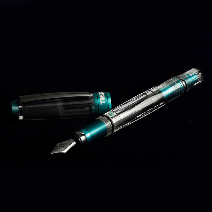 Dramatic lighting on the uncapped TWSBI Diamond 580ALR Caribbean Blue fountain pen against a dark background, emphasizing the striking contrast between the bright blue ribbed grip and black titanium nib.