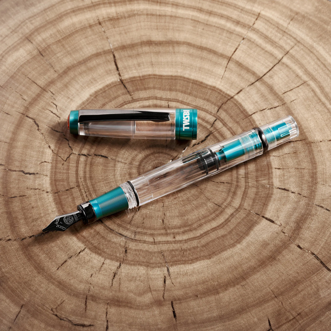 Uncapped TWSBI Diamond 580ALR Caribbean Blue fountain pen styled on a natural wood grain surface, perfectly showcasing the vibrant blue anodized aluminum and black titanium trim against the organic wood texture.