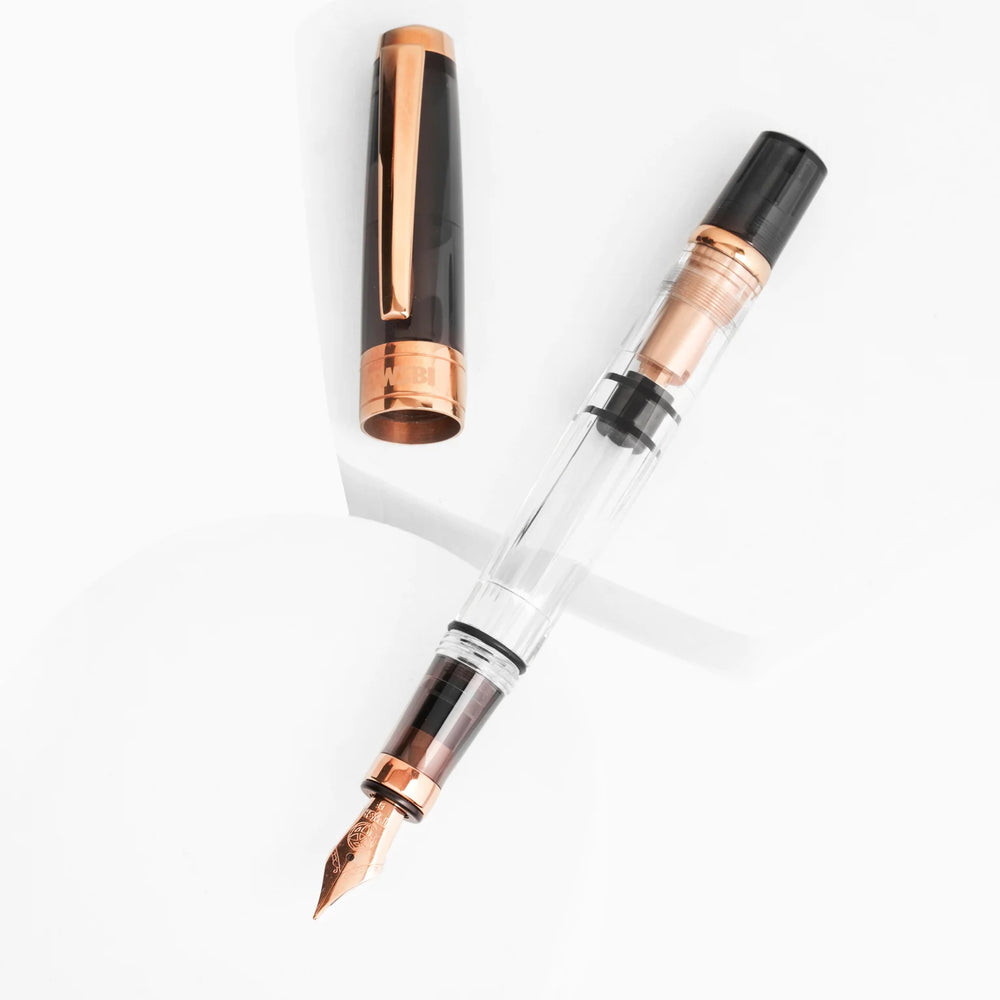 Artistic display of the TWSBI Diamond 580 Smoke RoseGold II fountain pen and cap resting on white geometric platforms, highlighting the striking contrast between the dark smoke resin, clear faceted barrel, and premium rose gold trim.