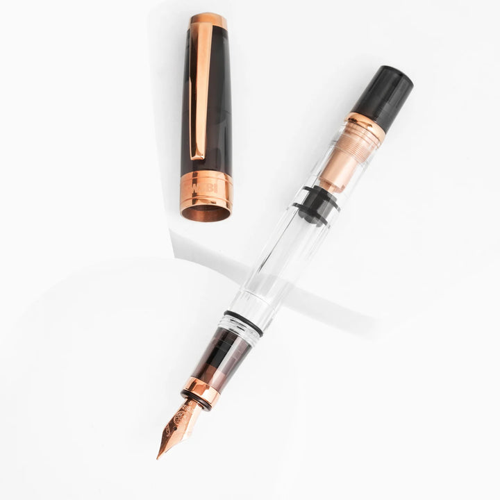 Artistic display of the TWSBI Diamond 580 Smoke RoseGold II fountain pen and cap resting on white geometric platforms, highlighting the striking contrast between the dark smoke resin, clear faceted barrel, and premium rose gold trim.