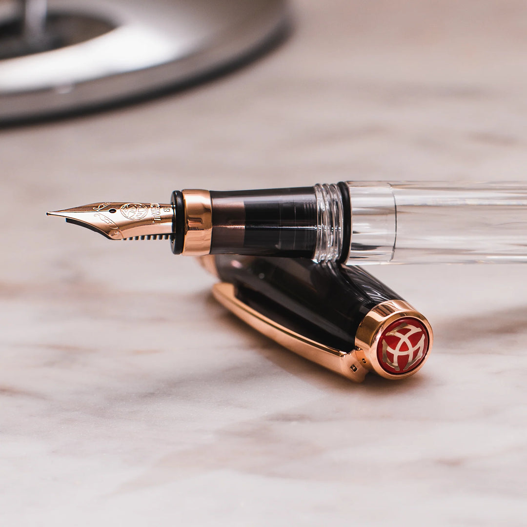 Close-up of the TWSBI Diamond 580 Smoke RoseGold II fountain pen resting on a marble surface, detailing the precision rose gold stainless steel nib, translucent smoke grip section, and the signature red TWSBI finial logo on the cap.