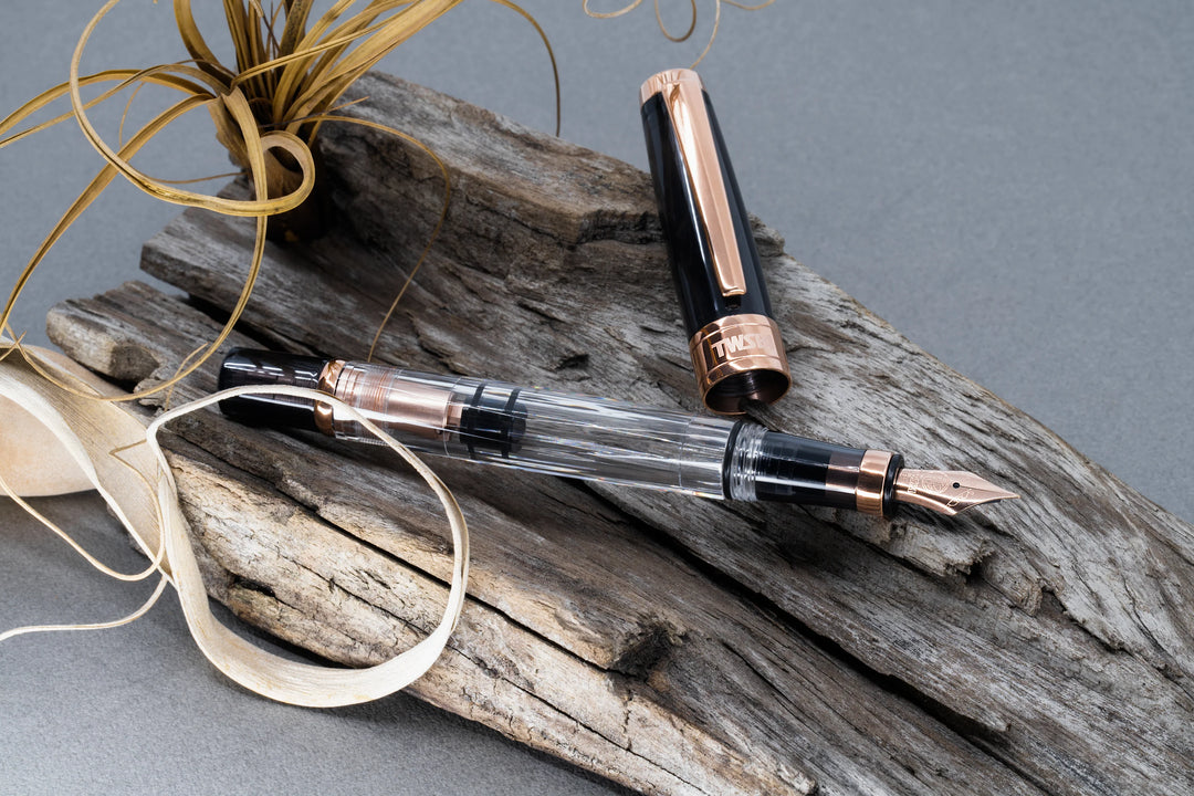 Uncapped TWSBI Diamond 580 Smoke RoseGold II fountain pen styled on weathered wood, displaying the clear ink barrel, internal rose gold piston filling mechanism, and matching smoke resin cap with a rose gold clip.