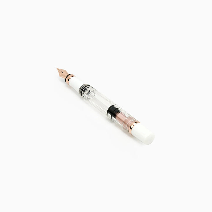 Angled view of the uncapped TWSBI Diamond 580 White Rose Gold II fountain pen, detailing the precision rose gold nib, crisp white grip section, and clear barrel revealing the internal black piston seal.