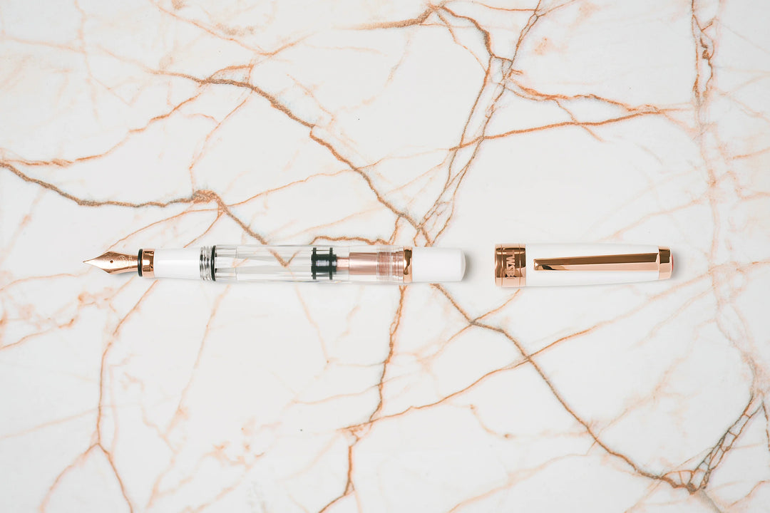 Overhead flat lay of the TWSBI Diamond 580 White Rose Gold II fountain pen and uncapped lid resting on white marble with rose gold veining, perfectly matching the pen's elegant white resin and rose gold-plated accents.