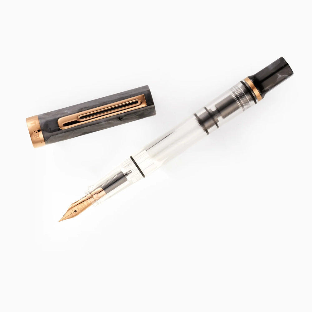 Top-down view of the uncapped TWSBI ECO Marble Bronze fountain pen and its detached cap arranged diagonally on a pure white background. The shot details the bronze-plated nib, internal piston mechanism, and the matching swirled black marble resin components.