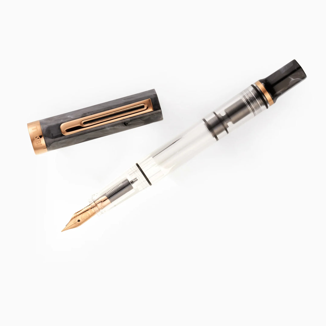 Top-down view of the uncapped TWSBI ECO Marble Bronze fountain pen and its detached cap arranged diagonally on a pure white background. The shot details the bronze-plated nib, internal piston mechanism, and the matching swirled black marble resin components.