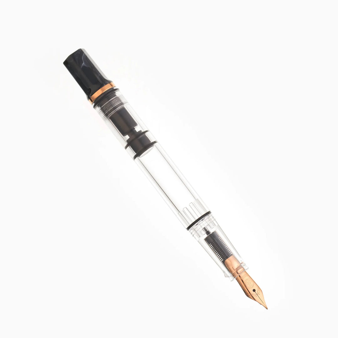 Uncapped, angled view of the TWSBI ECO Marble Bronze fountain pen resting on a seamless white background. The photograph highlights the bronze-plated steel Jowo nib, the clear high-capacity ink barrel, and the distinct swirled black marble resin piston knob.
