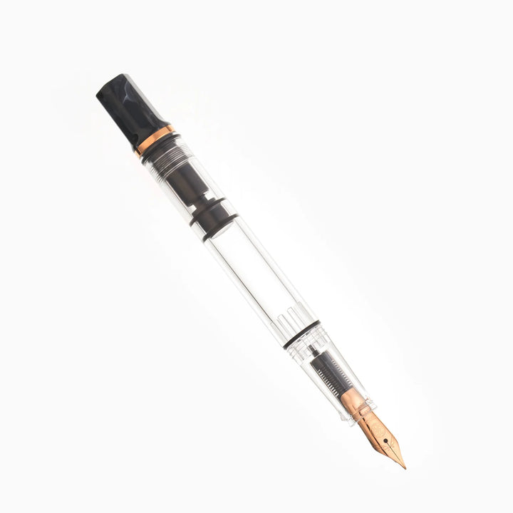 Uncapped, angled view of the TWSBI ECO Marble Bronze fountain pen resting on a seamless white background. The photograph highlights the bronze-plated steel Jowo nib, the clear high-capacity ink barrel, and the distinct swirled black marble resin piston knob.