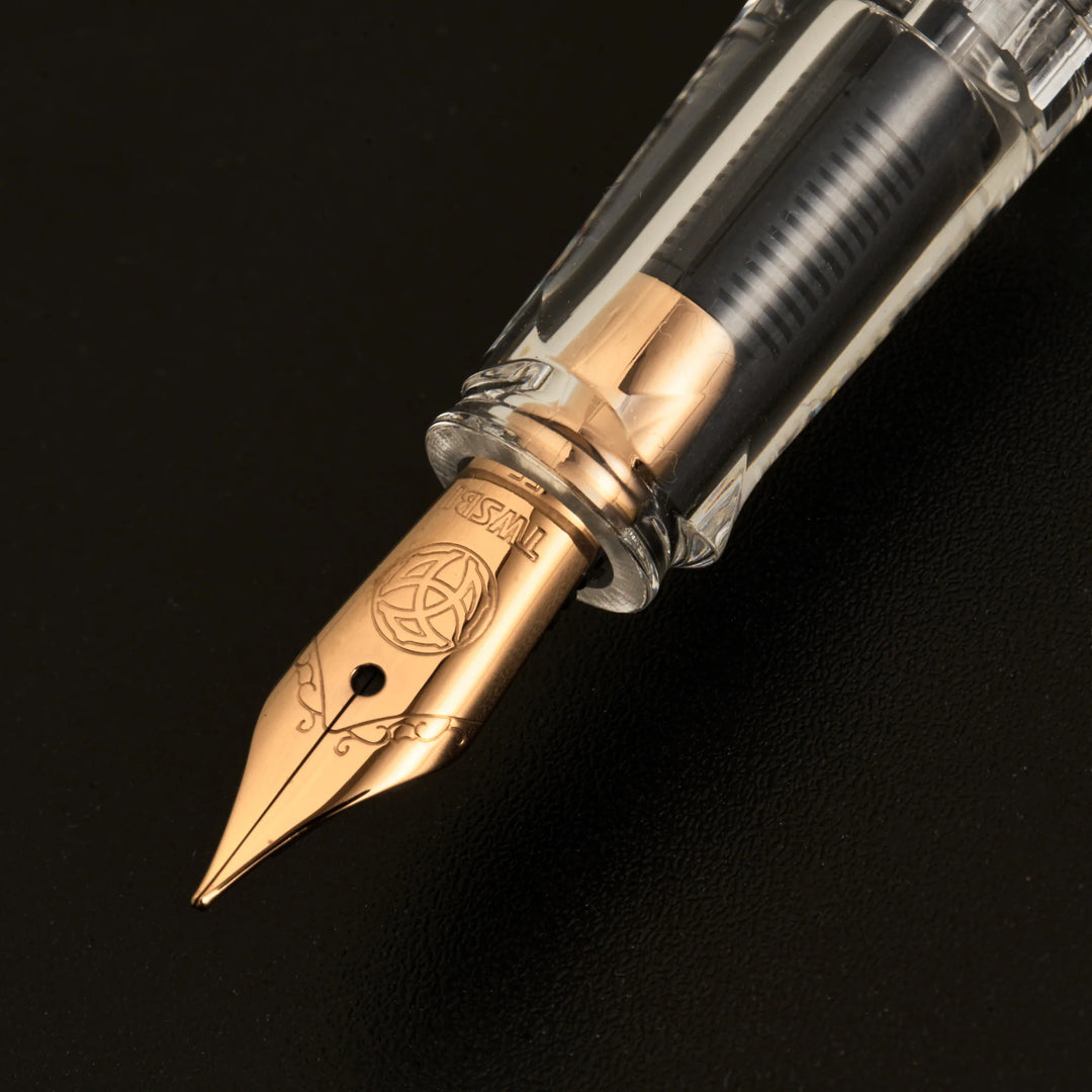 Macro product photograph of the uncapped TWSBI ECO Marble Bronze fountain pen on a dark background. The shot focuses intensely on the precision Jowo stainless steel nib, beautifully plated in warm vintage bronze, and the clear grip section showing the internal feed.