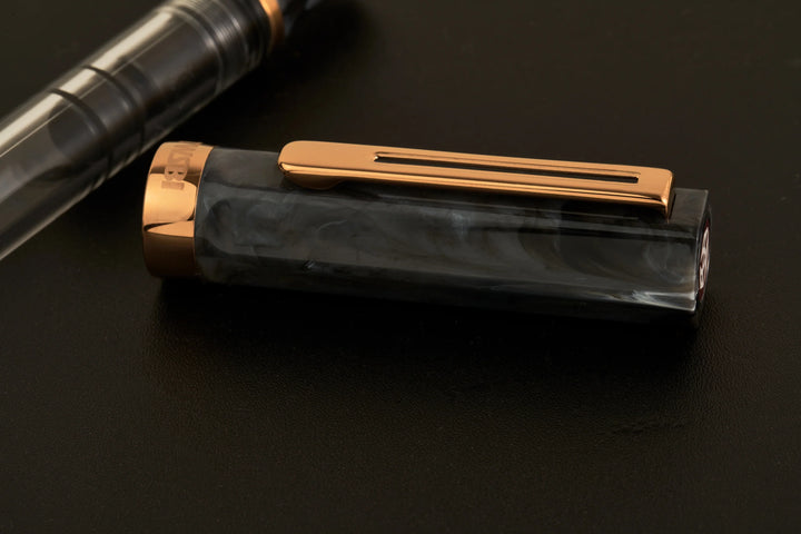 Detailed close-up of the detached cap from the TWSBI ECO Marble Bronze fountain pen resting horizontally on a dark surface. The image showcases the unique swirled black marble resin, the sleek bronze-plated pocket clip, and the bronze cap band engraved with the TWSBI logo.