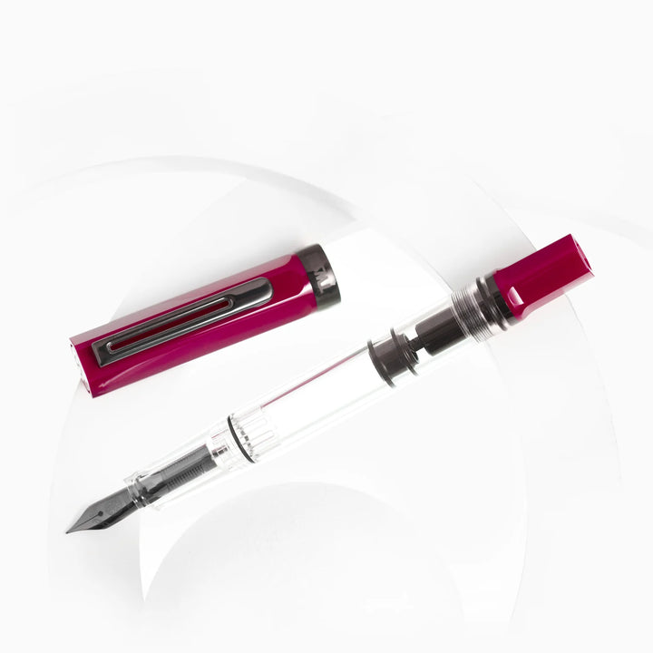 Top-down view of the uncapped TWSBI ECO Plum Onyx fountain pen and its detached cap arranged diagonally over subtle white acrylic display rings on a pure white background. The shot details the dark onyx-plated nib, the internal piston mechanism, and the deep plum purple resin components.