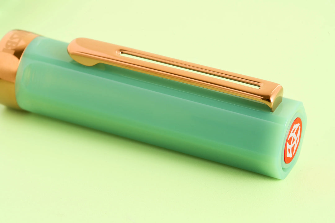 Macro close-up of the TWSBI ECO Jade Jelly fountain pen cap, highlighting the translucent milky green resin, bronze pocket clip, and red TWSBI finial logo.