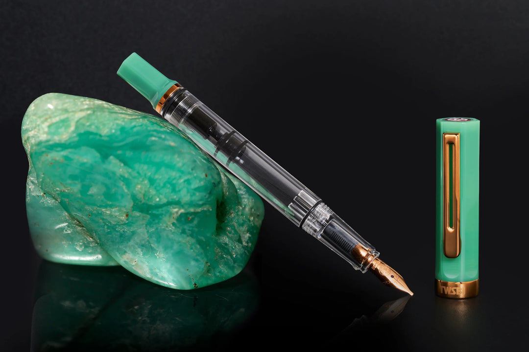 Editorial shot of the uncapped TWSBI ECO Jade Jelly Bronze fountain pen resting against a rough green gemstone on a reflective black background, showcasing the bronze-coloured nib.