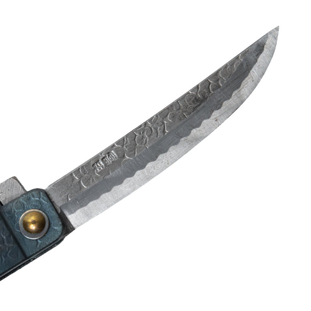 Macro close-up of the hand-forged Tomita blade, highlighting the Kengata profile, hammered spine, Japanese maker's mark, and characteristic Midareba wave pattern.
