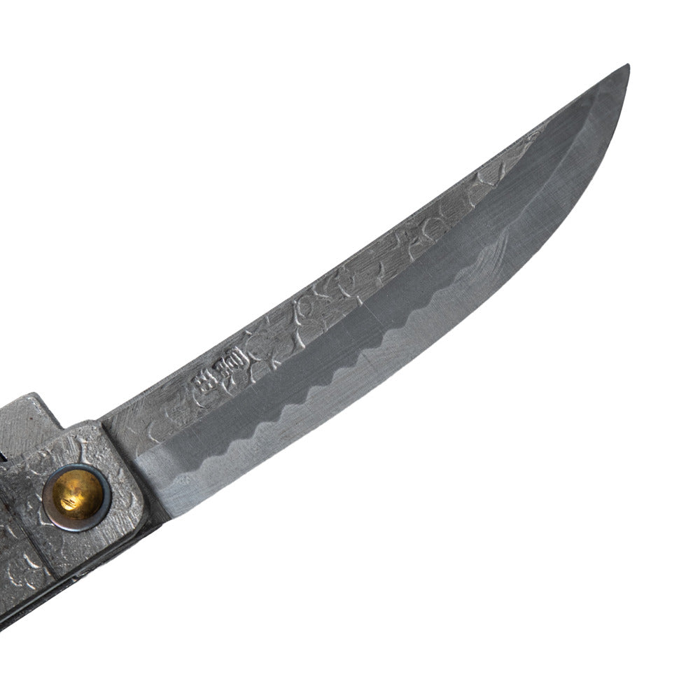 Macro close-up of the hand-forged Tomita blade, highlighting the Kengata profile, hammered spine, Japanese maker's mark, and characteristic Midareba wave pattern.