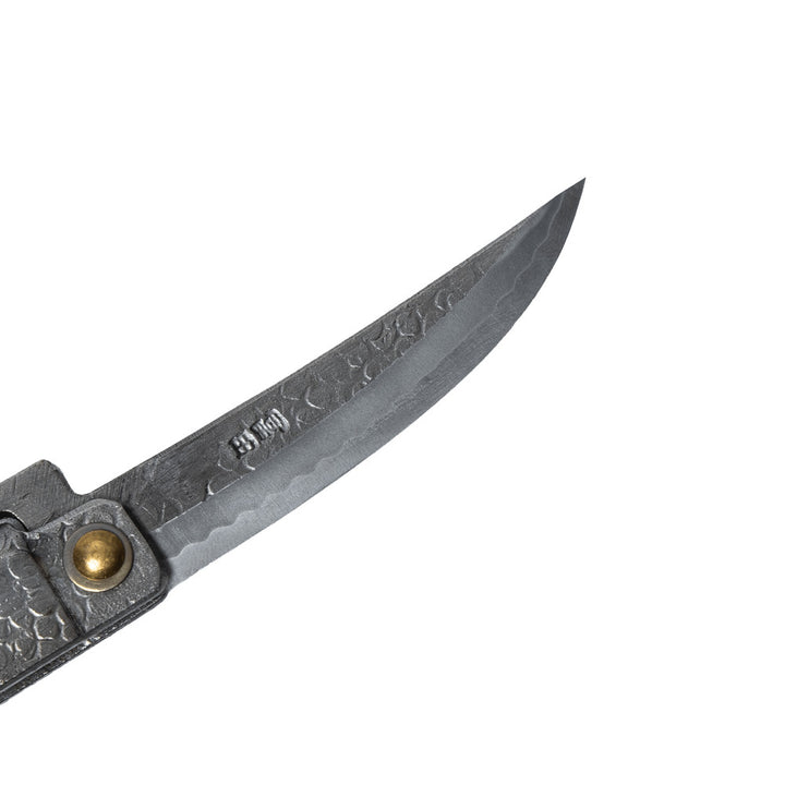 Macro close-up of the hand-forged Tomita blade, highlighting the hammered spine, Japanese maker's mark, and characteristic Midareba wave pattern.