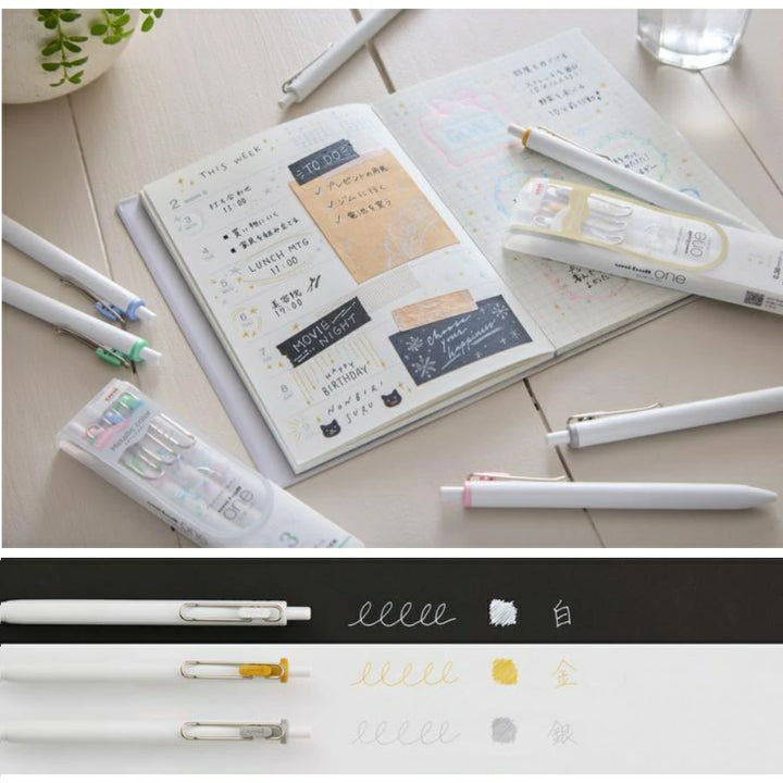 Bullet journal lifestyle scene demonstrating Uni-ball One Metallic Set performance on both black and white paper with Opaque White ink.