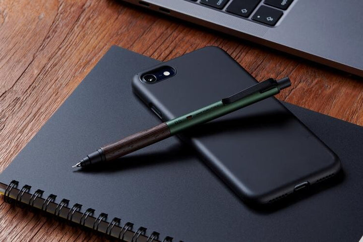 Uni Kuru Toga Wood 0.5mm mechanical pencil in Forest Green resting on a black notebook, highlighting the genuine Wenge wood grip and aluminum barrel.