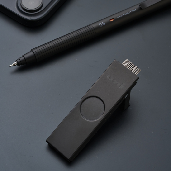 A premium stationery Everyday Carry (EDC) arrangement featuring the Uni Metal Lead Case in Limited Edition Matte Black with its thumb-slide open, revealing 40 pieces of 0.5mm graphite, paired with a matching Uni Kuru Toga Metal mechanical pencil on a sleek dark desk.