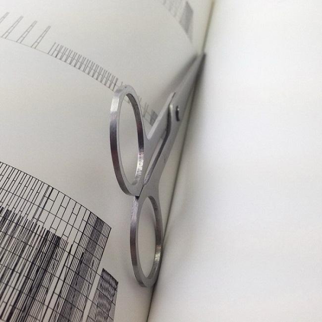 V-ROAD Ultra-Thin stainless steel scissors resting on an open book page, showcasing the tool's slim profile, large finger loops, and matte satin texture against the paper.