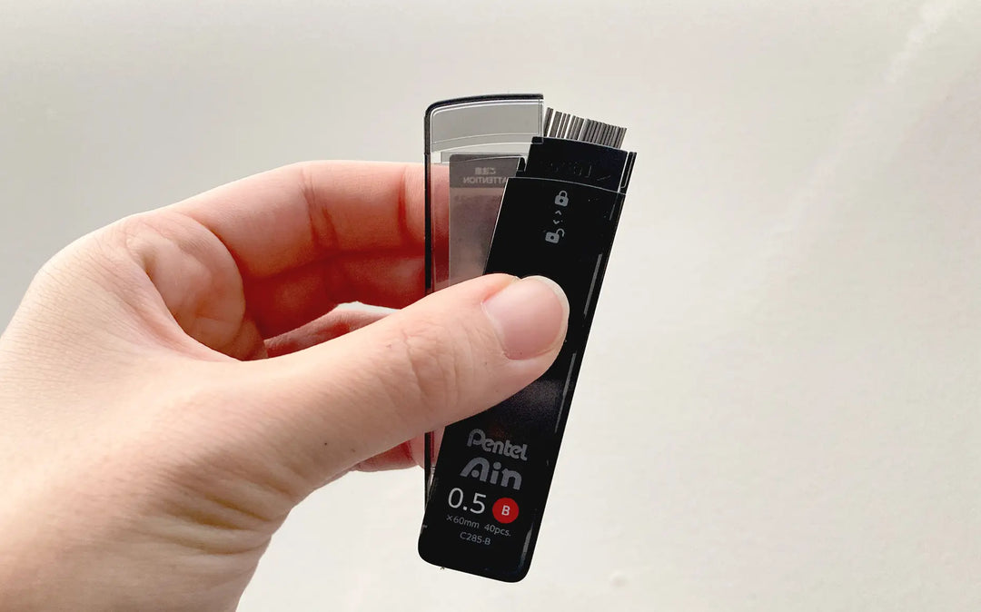 Close-up of Pentel Ain "Smart Slide" case mechanism. One-handed sliding lid design prevents spills and allows easy reloading of 0.5mm and 0.7mm leads.