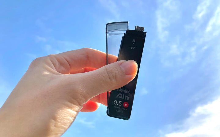 Close-up of Pentel Ain "Smart Slide" case mechanism. One-handed sliding lid design prevents spills and allows easy reloading of 0.5mm and 0.7mm leads.