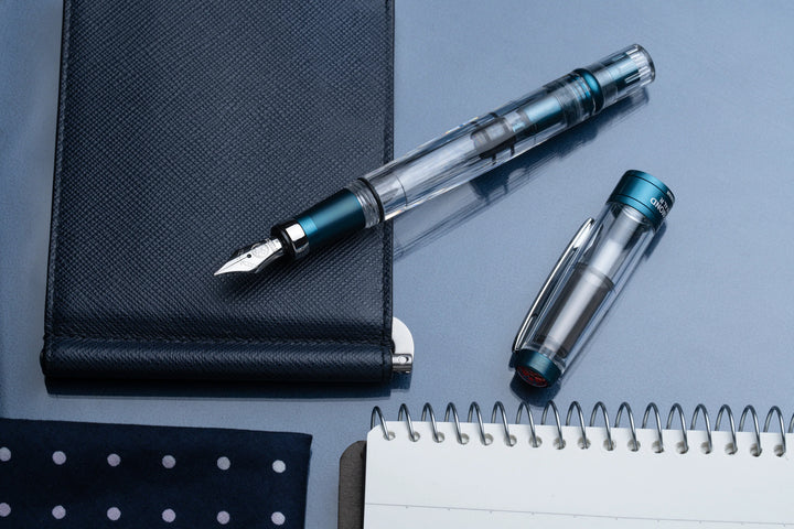 TWSBI Diamond 580ALR Fountain Pen – Prussian Blue on a reflective surface with a notebook.