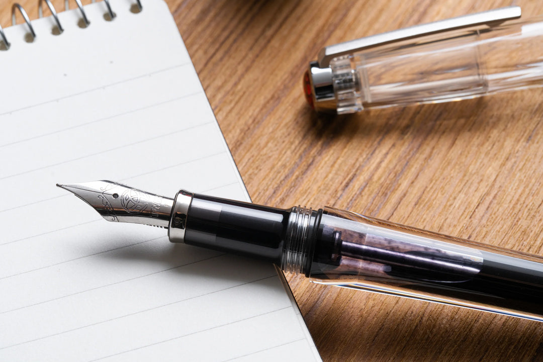 TWSBI Vac700R Fountain Pen - Clear on a wooden surface with a notebook